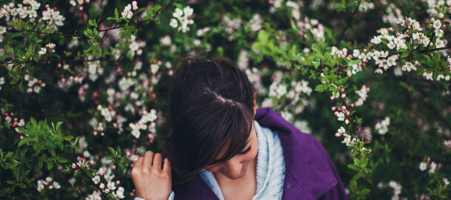 A woman walked through a row of flowering trees with pink buds and white petals on a background of green leaves