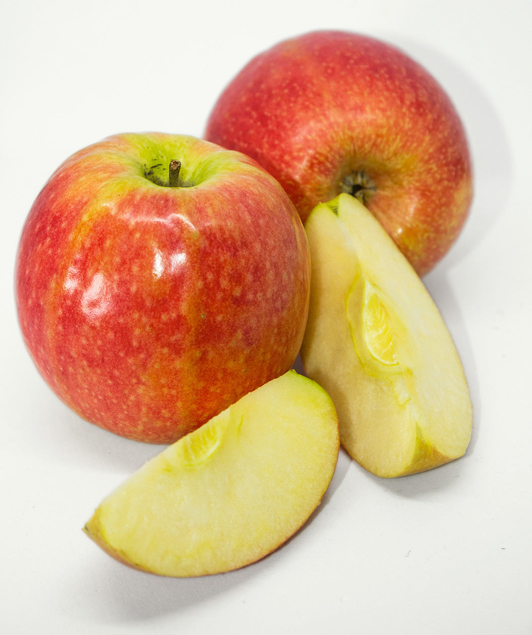 Pink Lady Apples on white, two round mostly red apples with light green blush and small white speckles along with a couple slices