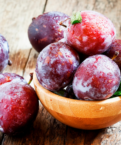 A wooden bowl of Santa Rosa Plums, various round redish-purple colored fruits