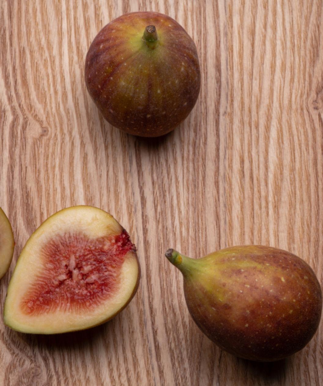 A couple Brown Turkey Figs on a table, round brown-green colored figs with 1 cut in half